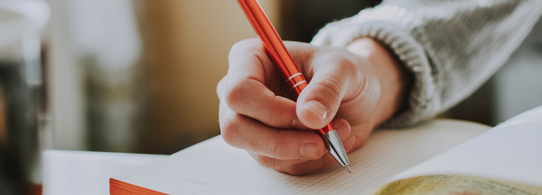 Hand holding a pen and writing in a notebook