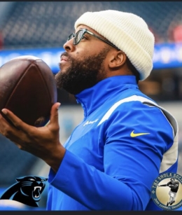 Man holding football in left hand and facing towards the left on a football field