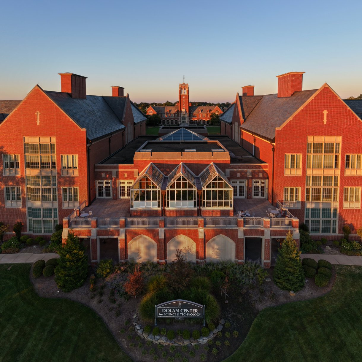 The grand red brick Dolan Center glows golden in the setting sun, with a wide lawn and patio for students to enjoy.