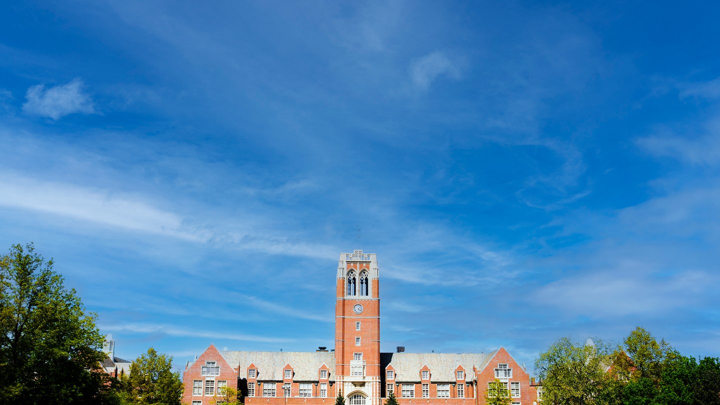 View of a large red brick campus building at John Carroll University with a central clock tower under a blue sky.