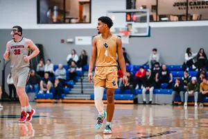 A basketball player wearing a gold uniform with number four walks on the court while another player in gray runs nearby.