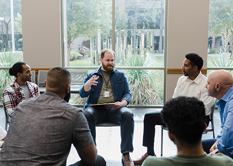 Men in group counseling session with counselor at center