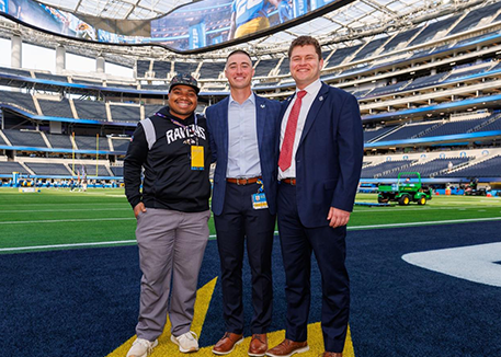 Picture of 3 males on NFL football field dressed in professional clothes before football game