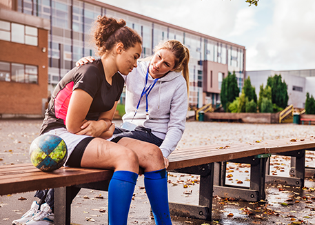 Female coach comforting female soccer player on bench outside