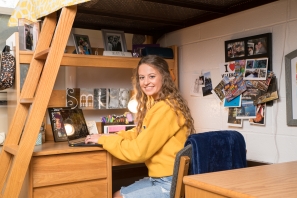 Student smiling and sitting at her desk in a residence hall room