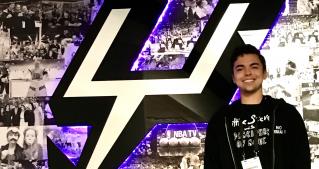 Brenan Betro stands in front of the San Antonio Spurs logo.