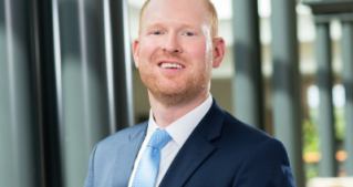 White ginger man with beard wearing a blue suit smiling at the camera