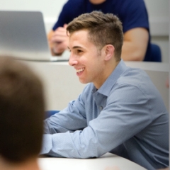 male student in blue shirt sitting at a desk smiling