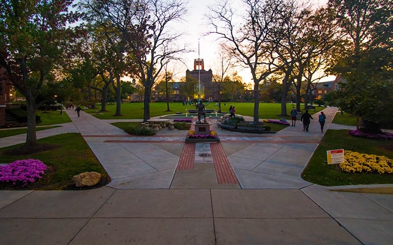 Campus photo at dusk showing the statue of St. Ignatius with the tower in the background and spring flowers everywhere 