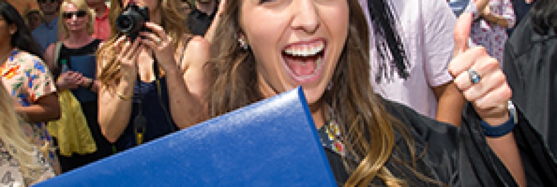 Happy female graduate giving a thumbs up in one hand and holding her diploma in the other