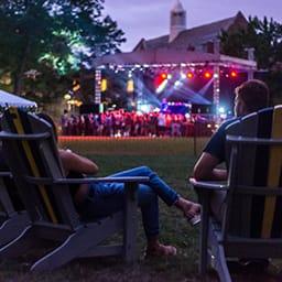 Image of students sitting in adirondack chairs watching a live concert on the quad