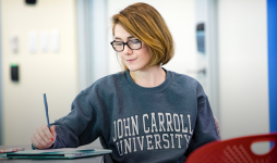 Female student wearing JCU sweatshirt sits in a classroom and writes. 