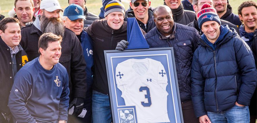 London Fletcher and his teammates surround a framed jersey and smile for the camera. 
