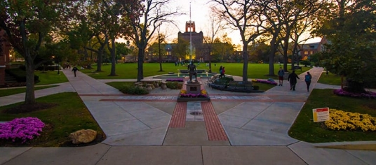 Campus photo at dusk showing the statue of St. Ignatius with the tower in the background and spring flowers everywhere 